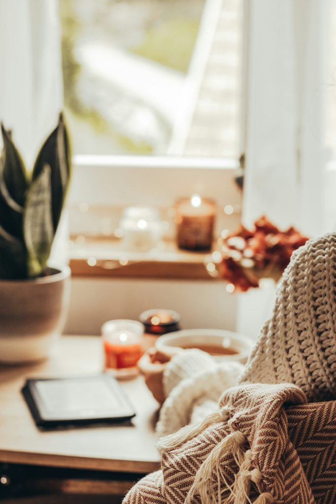 A person in a cosy knitted jumper holding a warm drink near candles, representing an autumn home refresh